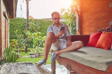 Yaz aylarında teras kanepede akıllı telefon kullanan adam.