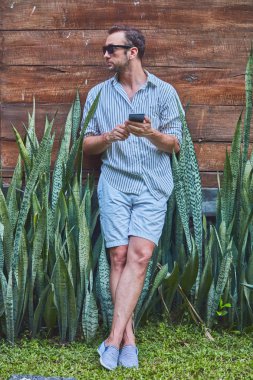 Akıllı telefon kullanarak güneş gözlüğü ve yazlık gömlek ile Man.