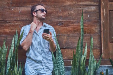 Akıllı telefon kullanarak güneş gözlüğü ve yazlık gömlek ile Man.