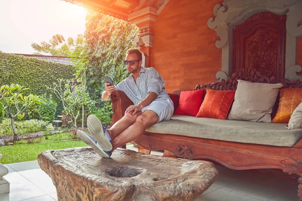 Hombre usando el teléfono inteligente en un sofá terraza en verano . — Foto de Stock