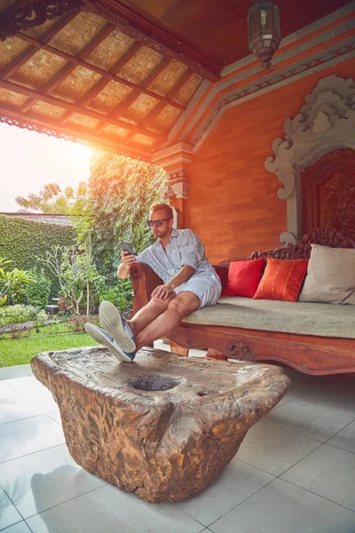 Hombre usando el teléfono inteligente en un sofá terraza en verano . — Foto de Stock