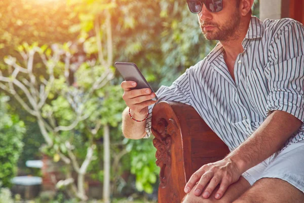Hombre usando el teléfono inteligente en un sofá terraza en verano . — Foto de Stock