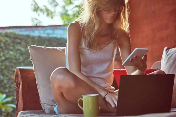 Жінка використовує ноутбук, мобільний телефон і п'є каву на домашньому порфірі — стокове фото