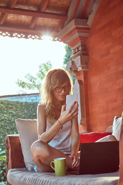Mujer usando laptop, celular y tomando café en un porc casero — Foto de Stock