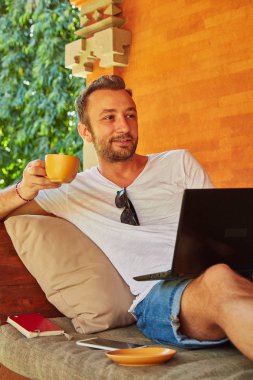 Bir ev verandada kahve / çay ve dizüstü bilgisayar ile Man.