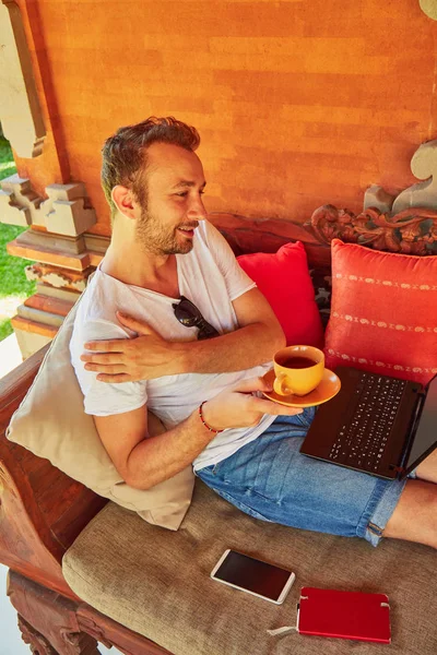 Hombre con café / té y portátil en un porche de casa . — Foto de Stock