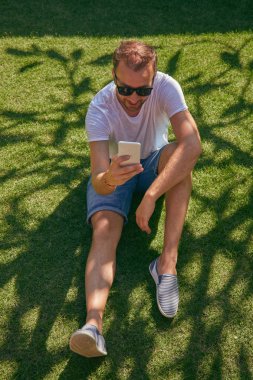 Summerti'de çimenlerde akıllı telefon kullanırken eğlenen adam