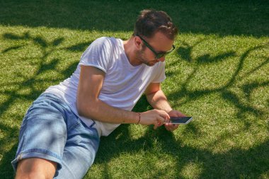 Summerti'de çimenlerde akıllı telefon kullanırken eğlenen adam