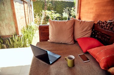 Dizüstü bilgisayar, cep telefonu ve kahve fincanı bir veranda kanepe açık havada toplam