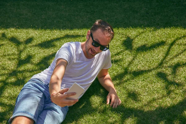 여름에 잔디에 자신의 스마트 폰을 사용하는 동안 즐기는 남자 — 스톡 사진