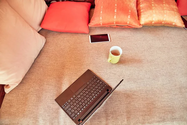 Laptop, cellphone and coffee cup on a porch sofa outdoors in sum — Stock Photo, Image