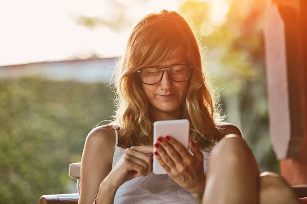 Mujer linda usando teléfono inteligente en un sofá porche . — Foto de Stock