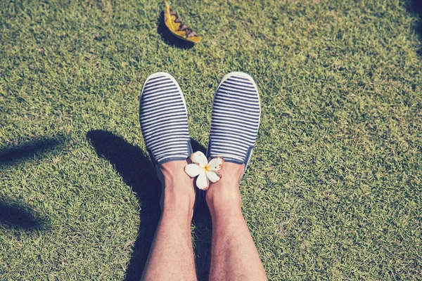 Man's feet with frangipani flowers on the green lawn.