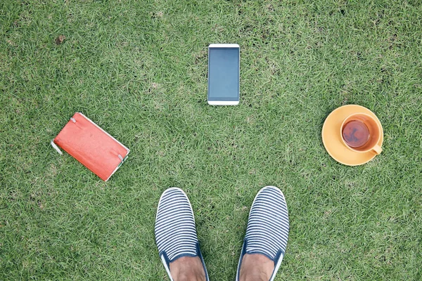 Hombre con teléfono inteligente, taza de café / té y portátil en una hierba —  Fotos de Stock