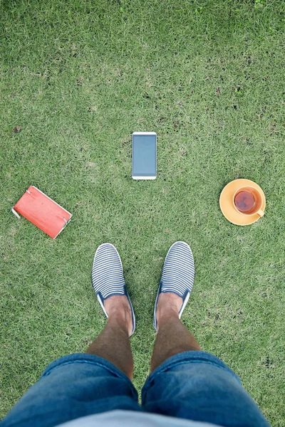 Άνθρωπος με smartphone, κούπα καφέ/τσάι και σημειωματάριο σε ένα γρασίδι — Φωτογραφία Αρχείου