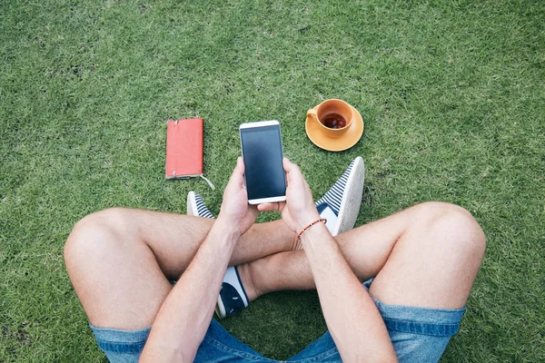 Hombre usando teléfono inteligente y beber café / té en una hierba . — Foto de Stock