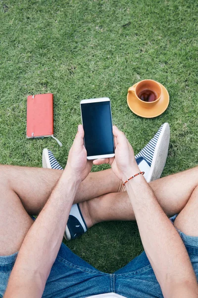 Hombre usando teléfono inteligente y beber café / té en una hierba . —  Fotos de Stock