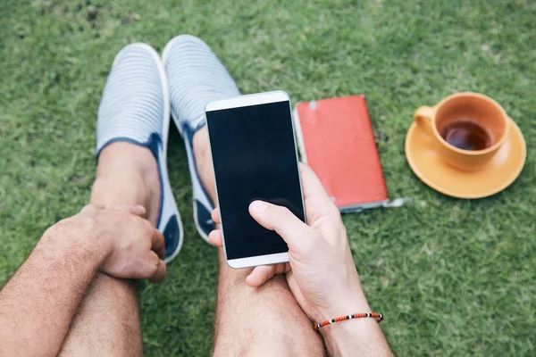 Hombre usando teléfono inteligente y beber café / té en una hierba . —  Fotos de Stock