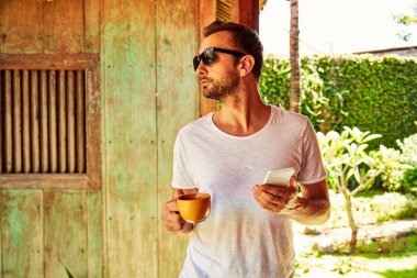 Bir evin önündeki verandada cellpohne kullanan adam.