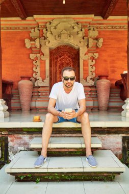 Bir evin önündeki verandada cellpohne kullanan adam.