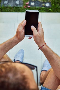 Bir evin önündeki verandada cellpohne kullanan adam.