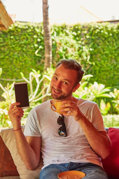 Hombre con café / té y teléfono celular en un porche casero . — Foto de Stock