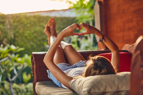 Girl holding a heart-shape symbol while lying on the couch. — Stock Photo, Image