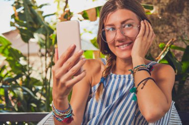 Bir terasta cep telefonu kullanarak gözlüklü sevimli kız.