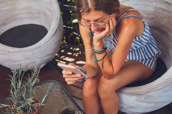 Симпатична дівчина в окулярах використовує мобільний телефон на терасі . — стокове фото