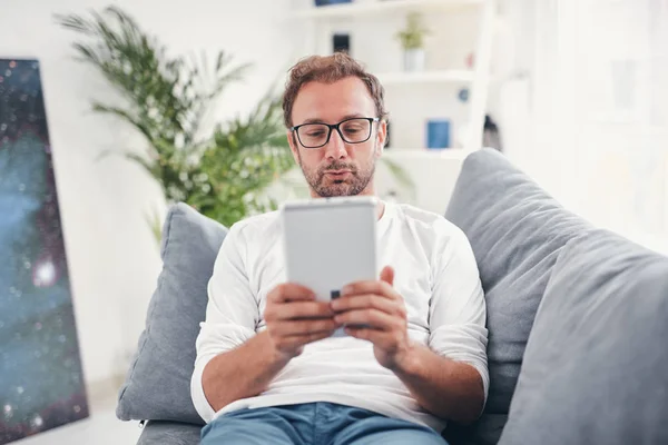 Hombre usando tableta y sufring en el Internet en su sala de estar . — Foto de Stock