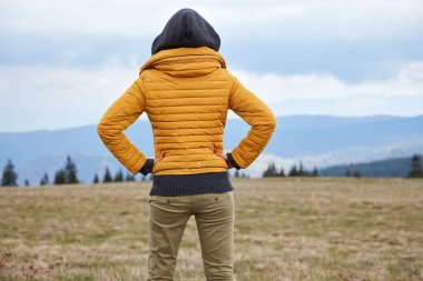 Kadın doğanın tadını çıkarıyor, arka planda tepe manzarası var..