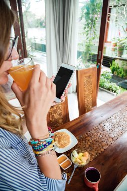 Modern genç kadın mutfakta cep telefonu kullanıyor..