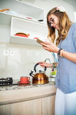 Modern genç kadın mutfakta cep telefonu kullanıyor..