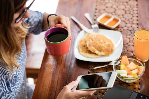 Woman using laptop and cellphone at home during breakfast - freelancing concept.