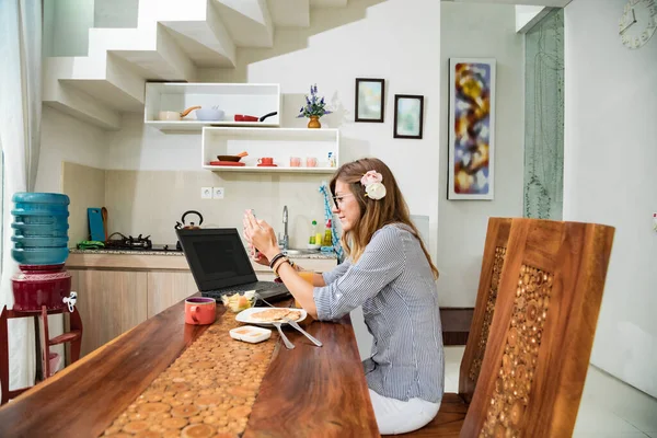 Woman using laptop and cellphone at home during breakfast - freelancing concept.