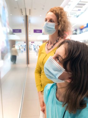 Anne ve kızı, salgın ve salgın durumunda korunmak için koruyucu tıbbi maskelerle alışveriş merkezinde..