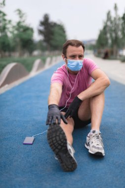 Tıbbi maskeli, eldivenli, akıllı telefonlu ve kulaklıklı sporcu şehir içinde koşuyor..