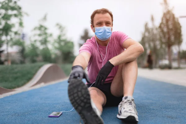 의료용 마스크와 장갑을 스마트폰과 이어폰을 사용하고 환경에서 조깅을 — 스톡 사진