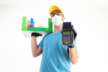 Koruyucu maskeli teslimatçı. Bakkaliye ve POS 'la dolu bir çanta tutuyor..