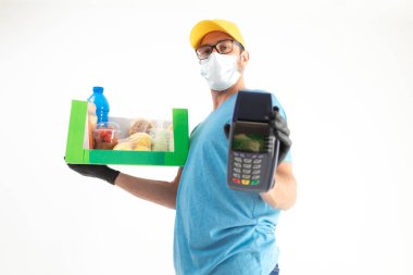 Koruyucu maskeli teslimatçı. Bakkaliye ve POS 'la dolu bir çanta tutuyor..