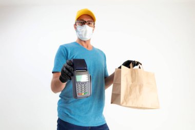 Koruyucu maskeli teslimatçı. Bakkaliye ve POS 'la dolu bir çanta tutuyor..