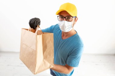 Koruyucu maskeli teslimatçı. Elinde poşet dolusu yiyecek var..