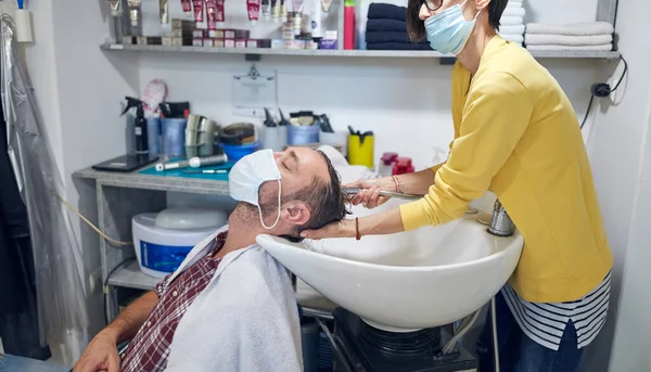 Hairdresser and customer in a salon with medical masks during virus pandemic. Working with safety mask.