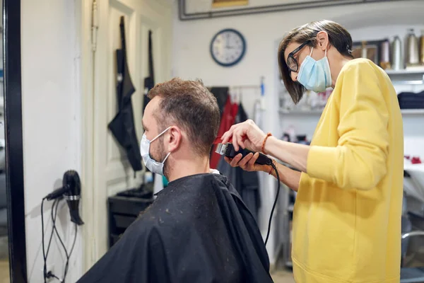 Hairdresser and customer in a salon with medical masks during virus pandemic. Working with safety mask.