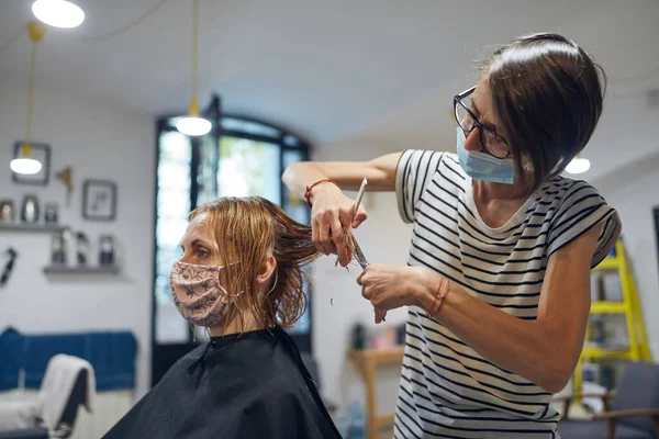 Hairdresser and customer in a salon with medical masks during virus pandemic. Working with safety mask.