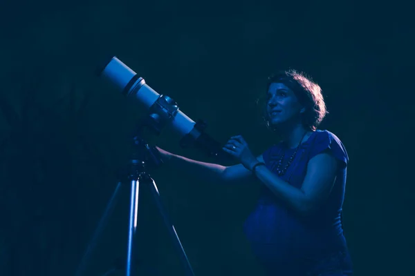 Pregnant woman looking at the stars through a telescope- astrology concept, horoscope predictions about the baby.