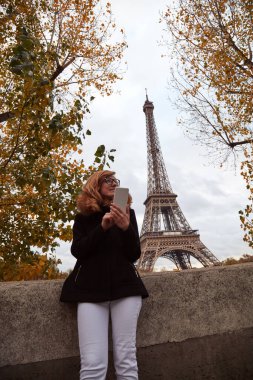 Paris geçmişi olan cep telefonu kullanan bir kız, Seine nehri ve Eyfel kulesi..