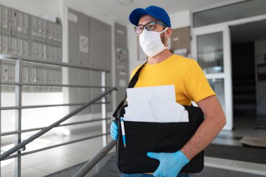 Postacı, virüs salgını sırasında posta çantası, koruyucu maske ve eldiven taşıyor..