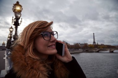 Paris geçmişi olan cep telefonu kullanan bir kız, Seine nehri ve Eyfel kulesi..