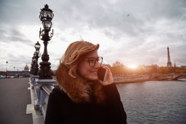 Paris geçmişi olan cep telefonu kullanan bir kız, Seine nehri ve Eyfel kulesi..